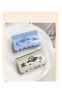 Detail view of two ocean-themed hair claws featuring blue and white shells and coral patterns