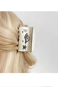 Detail of cream-colored claw clip with black ocean patterns on blonde hair