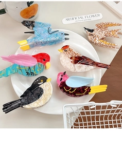 Close-up of bird-shaped acetate hair claws in various marble patterns on a white plate