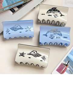 Macro detail of large ocean themed acetate hair claws with blue whale and shell patterns
