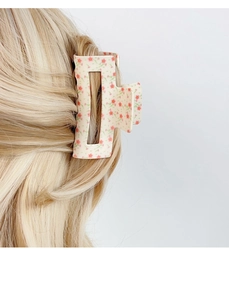 Detailopname van de holle vierkante haarklem met bloemmotieven op blond haar