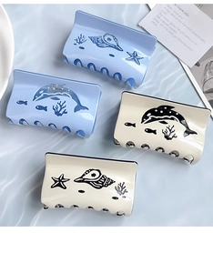 Close-up of ocean-themed hair claws with dolphin and seashell prints on blue water background