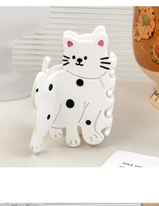 Détail d'une pince à cheveux chat en acétate crème avec pois noirs sur un fond de décor épuré