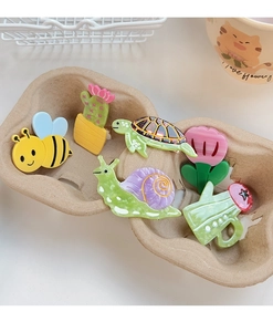 Detailed view of colorful bee, turtle and cactus hair clips in a textured tray