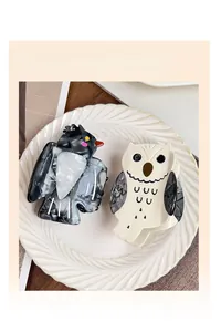 Close-up of cute cartoon owl hair claw clips with marble texture on white plate