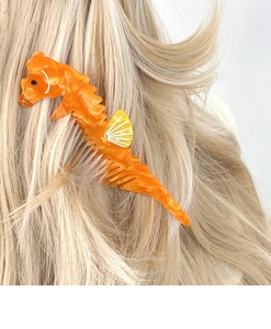 Detail of an orange seahorse hair comb with marble texture in blonde hair