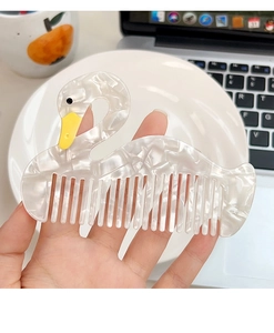 Detail of white marble-pattern swan hair comb with yellow beak held in hand