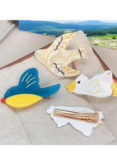 Detailed close-up of bird-shaped acetate hair clips with golden metal duckbill buckles