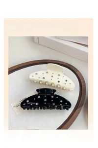 Detail of cream white and black hair claws with rhinestones on a woven tray