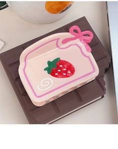 Détail d'une pince à cheveux en acétate avec fraise et nœud rose sur fond chocolaté