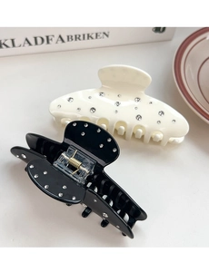 Detailed view of cream and black hair claws with sparkling rhinestones on white surface