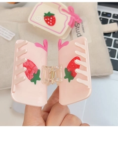 Gros plan d'une pince à cheveux rose en acétate avec fraise et nœud tenue à la main