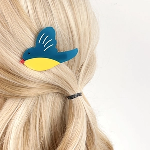 Cute bird-shaped acetate hair clip in blue and yellow on blonde hair, stylish hair accessory