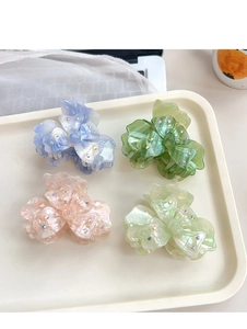 Détail de quatre pinces à cheveux trèfle pastel ornées de strass étincelants sur un plateau