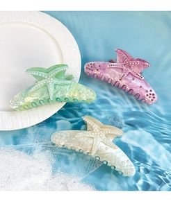 Detail of acrylic starfish hair claw clips with pearls on marble texture background
