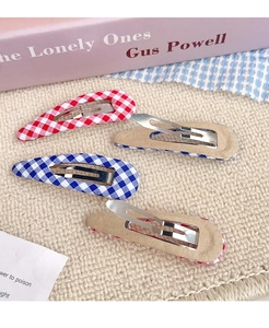 Detail of red and blue plaid fabric BB hair clips set on a pink book backdrop