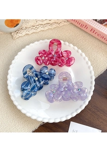 Detail of three floral acetate hair claws with rhinestones in pink, blue and purple