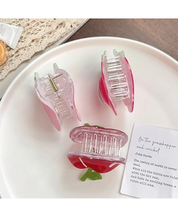Detailed view of three strawberry-shaped hair claws in red and pink with green leaf accents