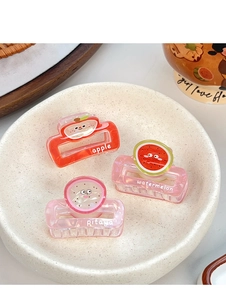 Close-up of fruit-shaped hair claws including apple and watermelon designs in a ceramic tray