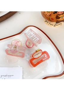 Detail of cute acrylic fruit hair claws including watermelon and apple designs in a ceramic plate