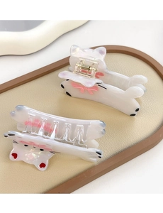Détail de deux pinces à cheveux chat blanc perle avec nœuds roses sur fond cuir beige