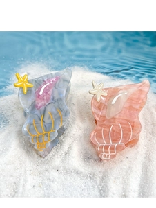 Close-up of shell-shaped acetate hair claws with starfish details on a beach sand background