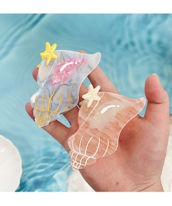 Close-up of conch and starfish acetate hair claws held over a sparkling blue pool water background