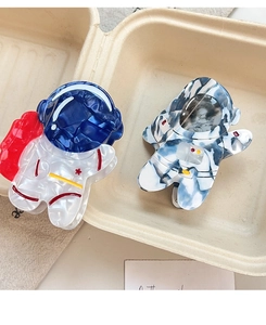 Detail of two astronaut-shaped acetate hair claws in blue and white marble textures