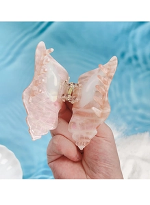 Detail of pink pearlescent butterfly hair claw clip held over a summer blue water background
