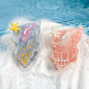 Chic acetate sea shell hair claws with starfish detail on a sandy beach setting
