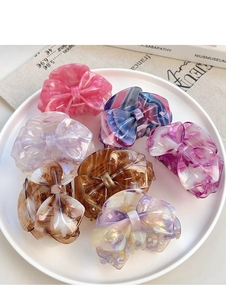 Detail showing bow-knot hair clips in seven assorted colors on a ceramic plate