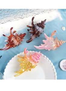 Détail de pinces à cheveux en forme de coquillage coloré avec fini irisé sur sable