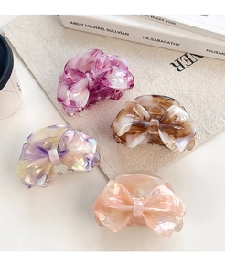 Detail view of four marble-patterned bow hair claws in purple, brown, and pink tones