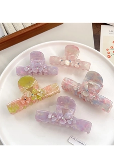 Close-up of five floral acetate hair claws with rhinestones on a white ceramic tray