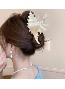 Détail d'une pince à cheveux irisée en forme de conque portée sur un chignon latéral
