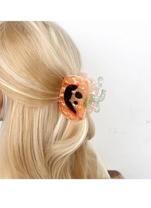 Gros plan d'une pince à cheveux citrouille avec texture marbrée orange sur cheveux blonds