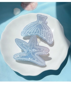 Macro view of gradient blue starfish and mermaid tail hair clips on a white plate