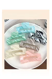 Detailed view of six colorful large striped hair claw clips on a white ceramic plate