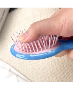 Detail of high-elasticity pink air cushion being pressed on a marble pattern hair comb