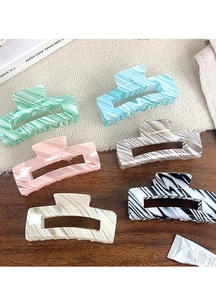 Detail shot of rectangular hair claws with marble and striped patterns on a textured desk