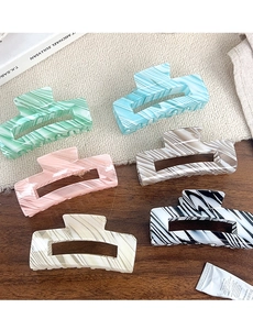 Detail of colorful marble pattern hair claws in pastel tones on a natural wooden table