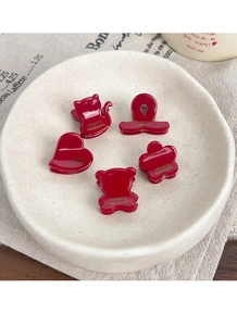 Detail of five vintage red acetate hair clips in cat, bear, and floral shapes on ceramic