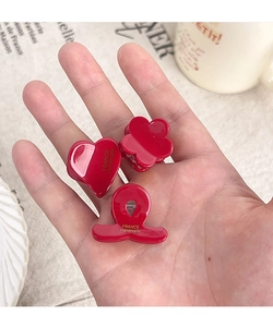 Close-up of three mini red hair clips in heart, flower, and wave shapes with gold logo