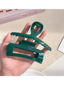 Macro detail of large dark green glossy hair claw clip held in hand with spring view