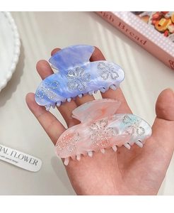 Detailed macro view of two marble hair claws with elegant rhinestone flower patterns