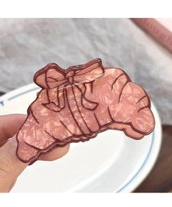 Gros plan d'une pince à cheveux en forme de croissant en résine ambre avec un petit nœud