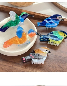 Detail shot of five colorful acetate bird hair claws with marbled texture on a wooden tray