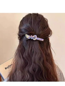 Dettaglio di un fermaglio a fiocco viola cangiante su lunghi capelli castani mossi