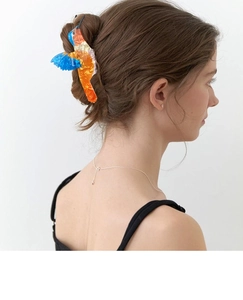 Detail view of a colorful bird hair claw clip in acetate on model's hair style