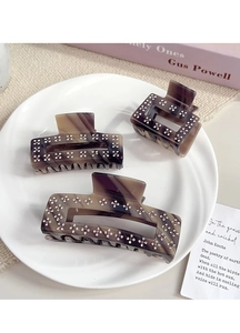 Close-up of tortoise shell acetate hair claws with rhinestones on a white ceramic plate